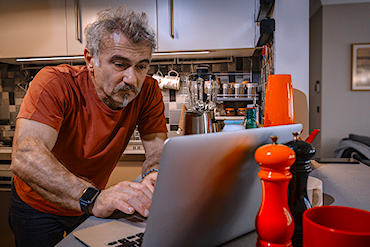 Man står lutad över sin dator som står på köksbänken