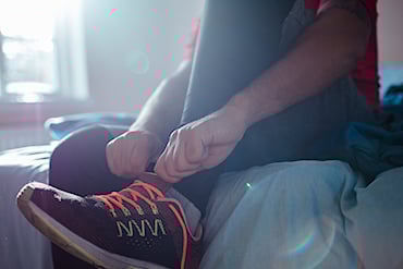 Person som sitter på sängkanten och knyter sina löparskor.