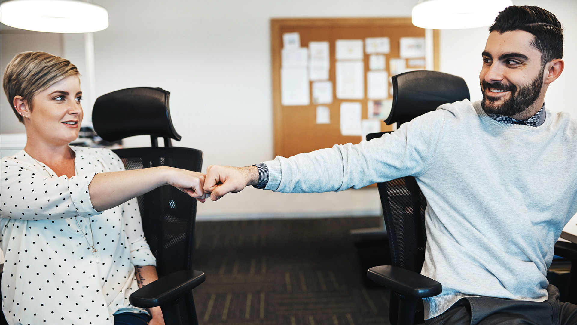 Två kollegor sitter på kontor och gör en fistbump för att visa samarbete.