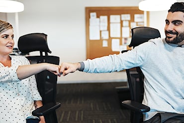 Två kollegor sitter på kontor och gör en fistbump för att visa samarbete.