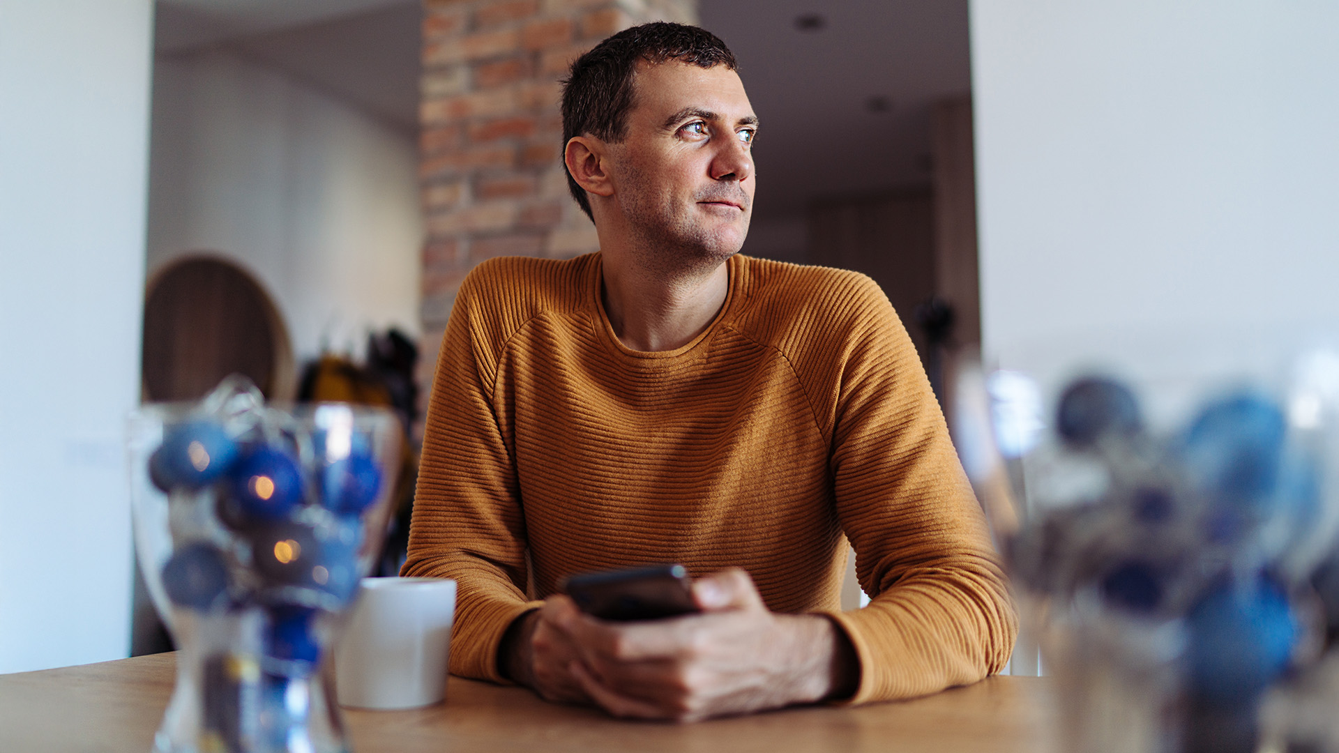 En man sitter i köket och använder en smartphone